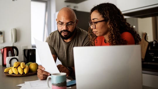 Man and woman review a document with an open laptop.